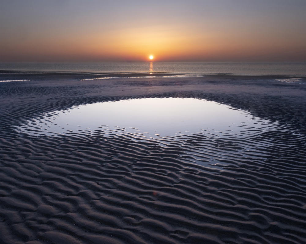 pattern in sand and colorful reflection of setting sun in water during sunset on beach