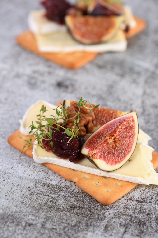 Cracker with a slice of camembert, jam, figs and nuts.A great snack idea for a holiday, picnic or party.