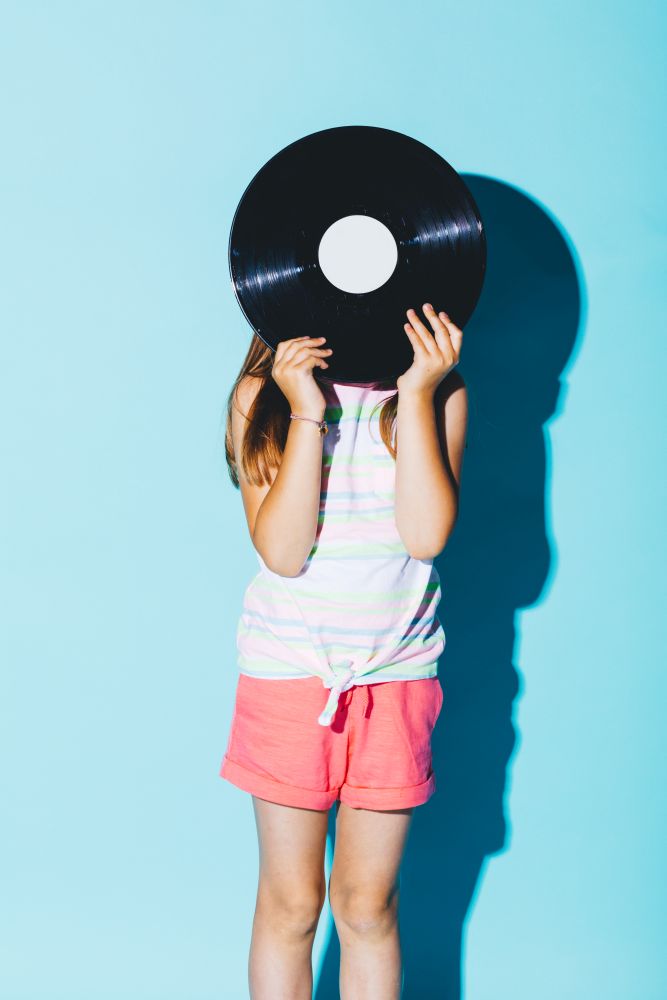 Little girl holding a vinyl disc against her head. Vintage technology. Childhood fun.. Little girl holding a vinyl disc against her head.
