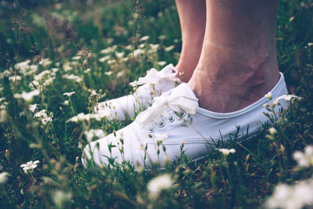 Woman in white sneakers standing on spring meadow with flowers. Feet close-up. Vintage.. Woman in sneakers standing on meadow with flowers.