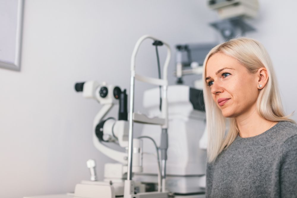 Woman sitting at the optician&rsquo;s office, modern medical equipment in the background. Oculist appointment.. Woman sitting at the optician&rsquo;s office