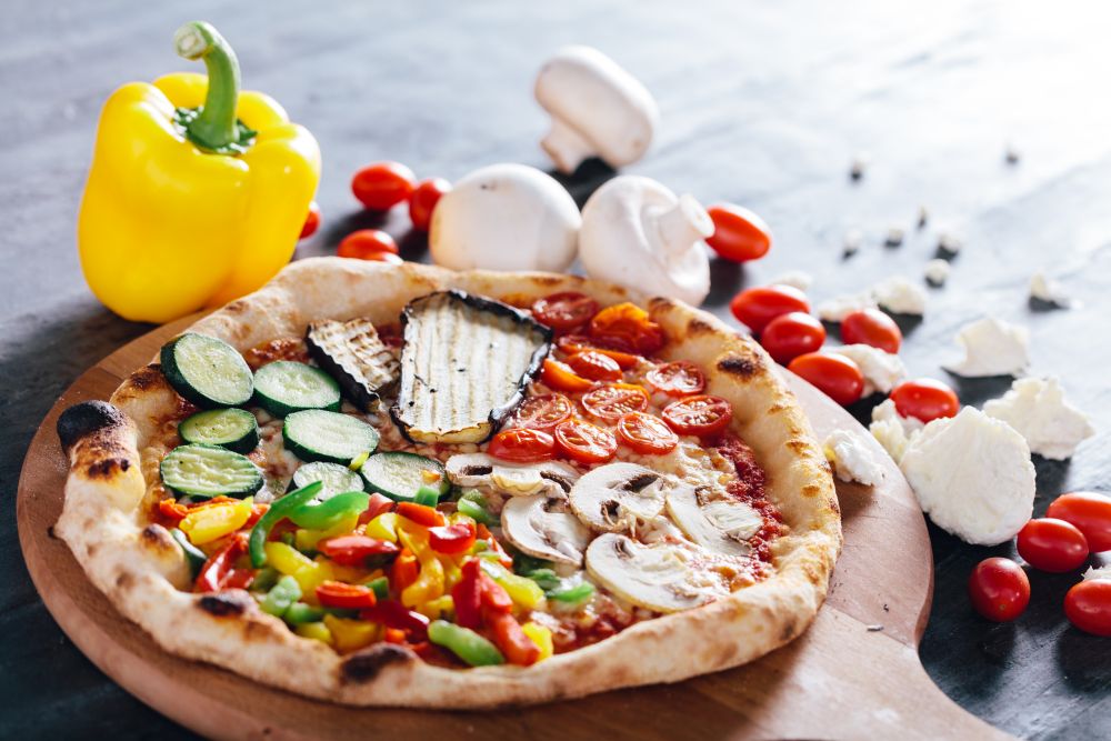 Pizza with tomatoes, mushrooms, grilled eggplant, pepper and zucchini on wooden board. Yellow pepper, mushrooms, mozzarella and tomatoes in the background. Vegetarian food.. Pizza with tomatoes, mushrooms, grilled eggplant, pepper and zucchini