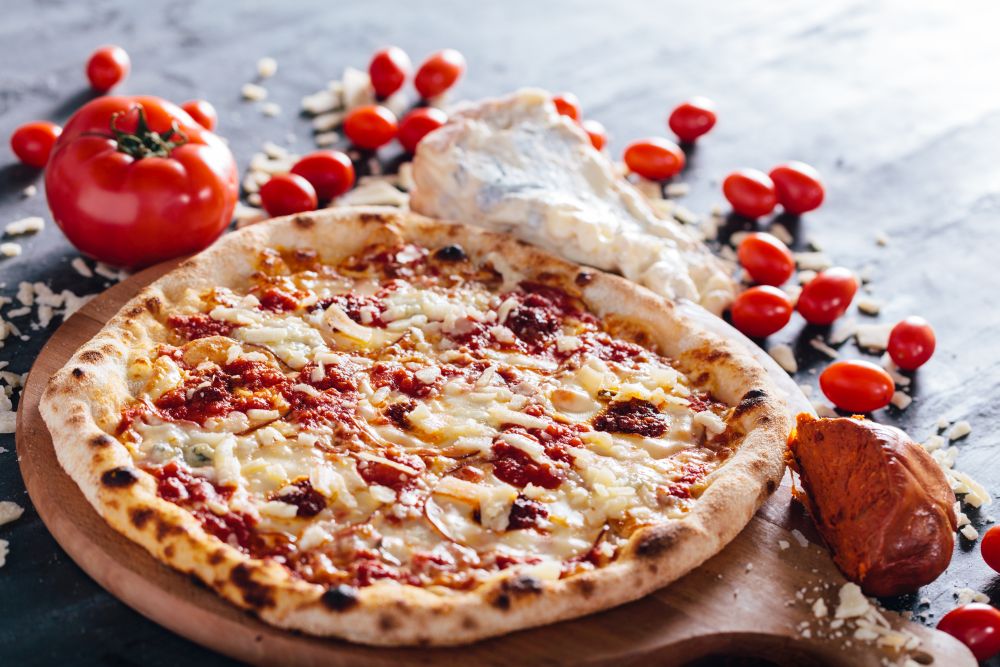 Pizza with meat spread, parmesan and blue cheese on wooden board. Meat spread, tomatoes, blue cheese and parmesan in the background. Popular Italian food.. Pizza with meat spread, parmesan and blue cheese