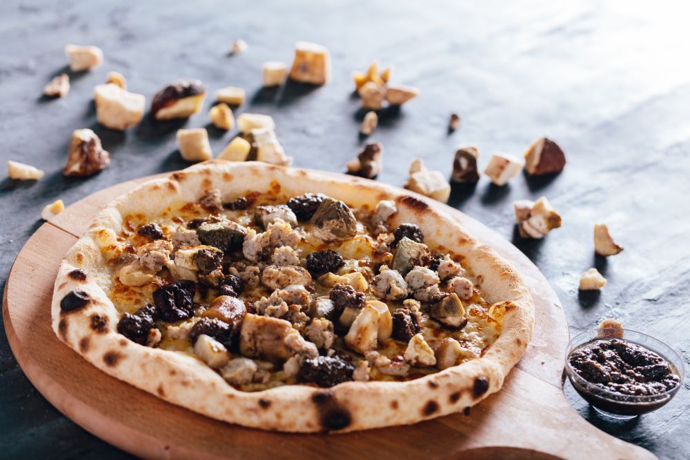 Pizza with porcini mushrooms, sausage and truffle sauce on wooden board. Porcini mushrooms and truffle sauce in the background. Popular Italian food.. Pizza with porcini mushrooms, sausage and truffle sauce