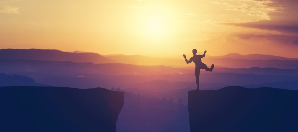 Man balancing on the edge of a cliff on a sunset sky. Adrenaline, danger, thread, vulnerabilty.. Man balancing on the edge of a cliff.