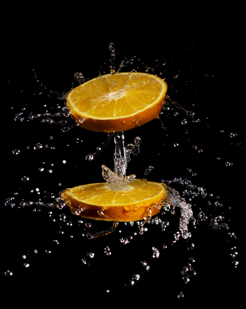 creative composition image of juicy orange slices spinning and splashing water isolated on black background