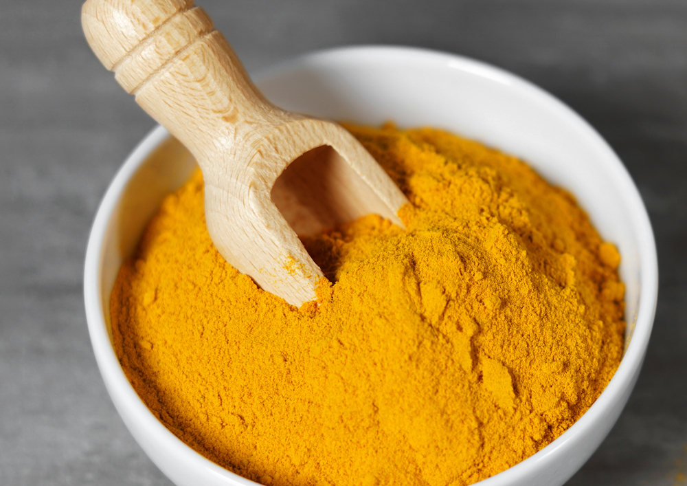Turmeric powder healthy spice Asian food closeup of a white bowl with a wooden bailer.