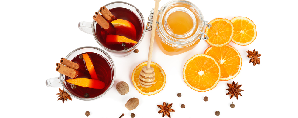 Hot red mulled wine, bee honey, slices of oranges and spices isolated on white background. Flat lay, top view. Free space for text. Wide photo.