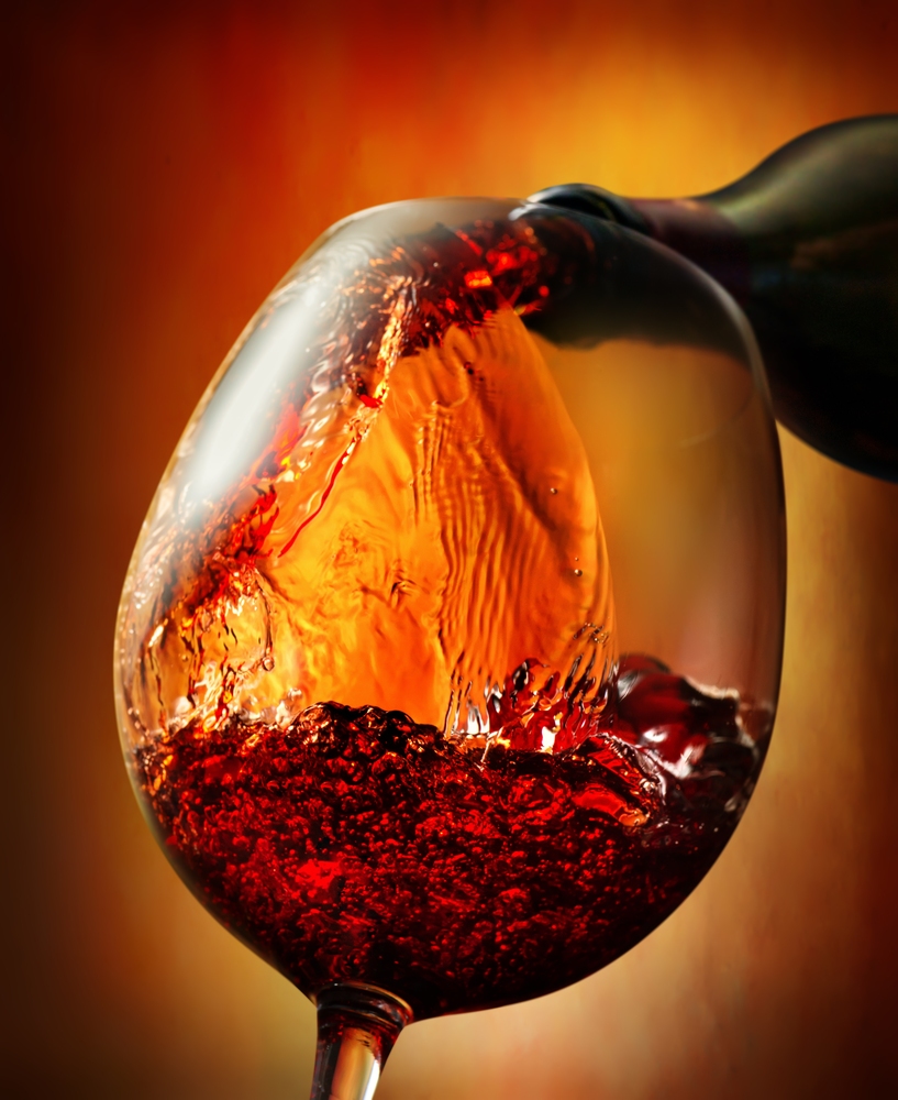 Red wine pouring into wineglass on an orange background