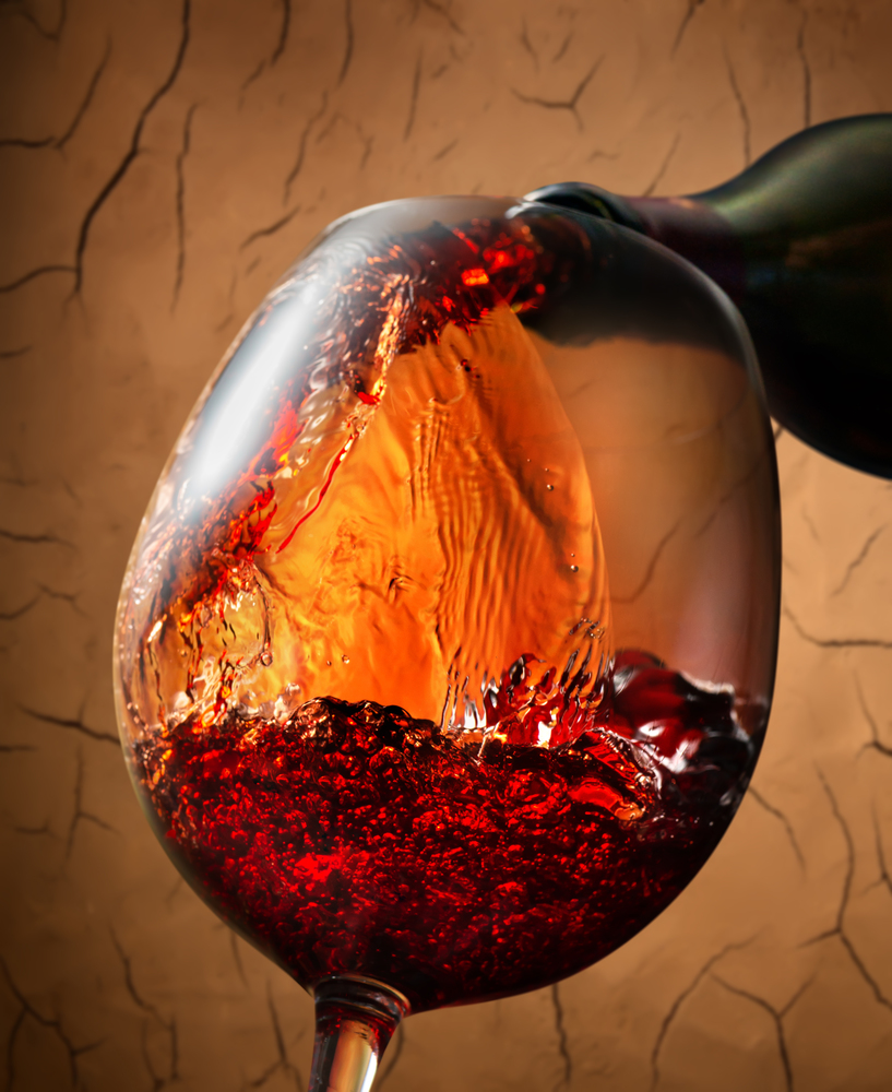 Red wine pouring into wineglass on clay background