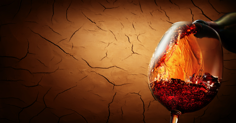 Wine pouring from bottle into wineglass on cracked clay background