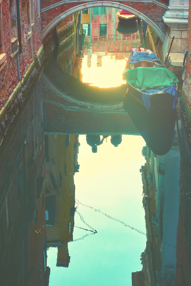 Venetian mirror - Houses, sunset sky and small bridge reflect in canals water, Venice