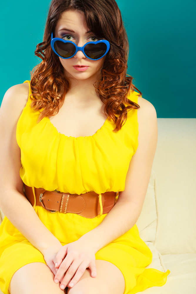Summer fashion eyes protection concept. Closeup girl long curly hair yeloow dress in blue heart shaped sunglasses