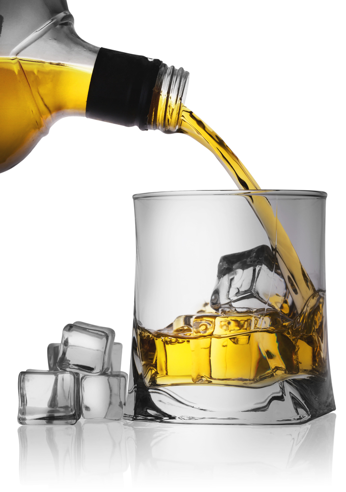 Whiskey pouring from the bottle into a glass with ice isolated on white background. Whiskey pouring from the bottle into a glass with ice