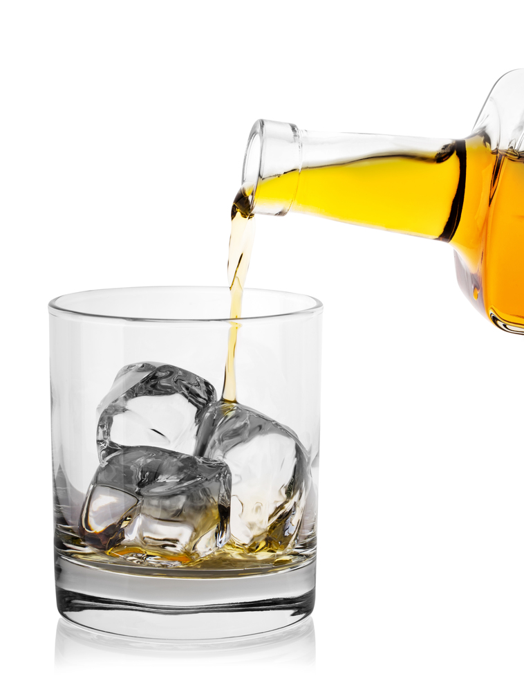 Pouring whiskey from a bottle into glass with ice isolated on white background. Pouring whiskey from bottle into glass with ice