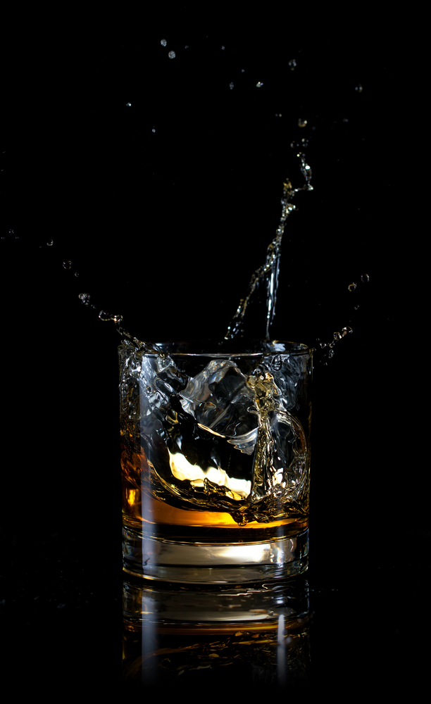 Splash of ice in glass of whiskey isolated on a black background. Splash of ice in glass of whiskey