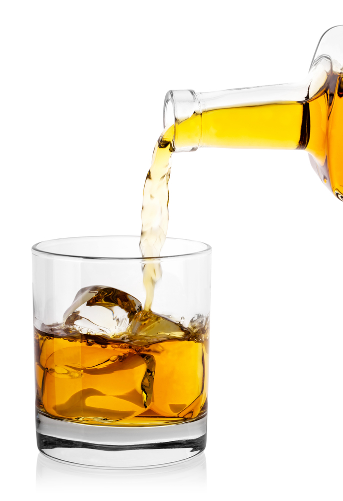 Whiskey from bottle poured into glass with ice cubes isolated on white background. Whiskey from bottle poured into glass with ice cubes