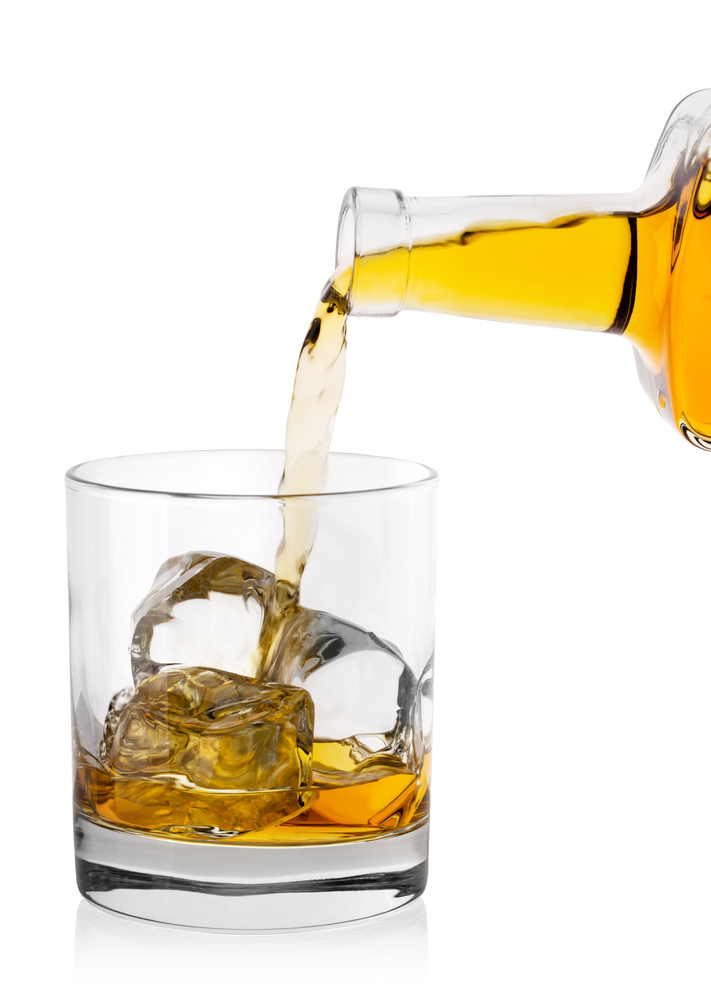 Whiskey pours from bottle in round glass with ice isolated on white background. Whiskey pours from bottle in round glass with ice