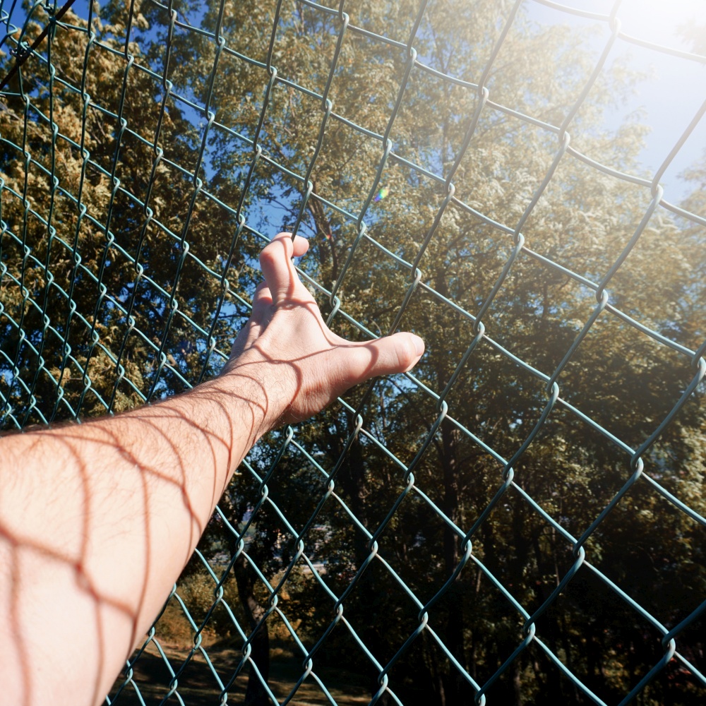 man hand grabbing metallic fence, feeling free