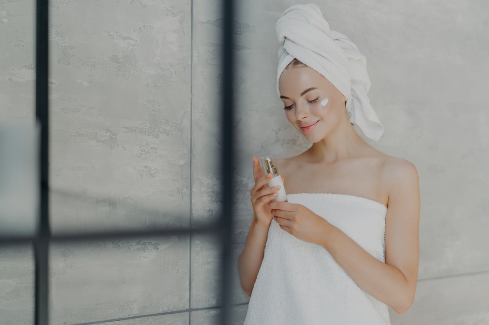 A serene woman in a towel examines a serum bottle in a spa-like bathroom