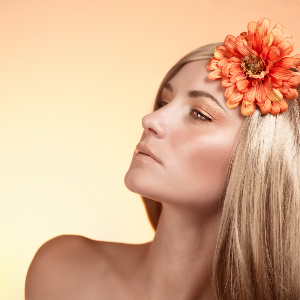 Closeup portrait of beautiful blond woman with orange flower in hair isolated on beige background, autumn season, beauty concept