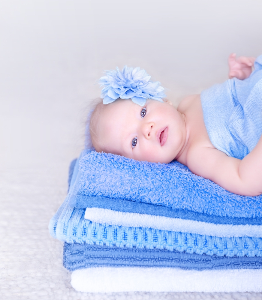 Sweet baby girl lying down on fresh soft blue towels with flower in head, stylish accessories for child, healthy lifestyle, happy childhood concept