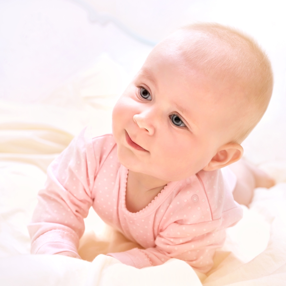 Closeup portrait of cute newborn baby lying down on the bed at home, wearing sweet pink clothes, purity and innocence concept