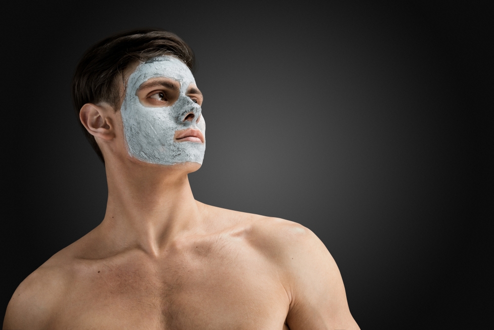 Portrait of a beautiful relaxed young man with a facial mud clay mask, face and body skin care treatment.