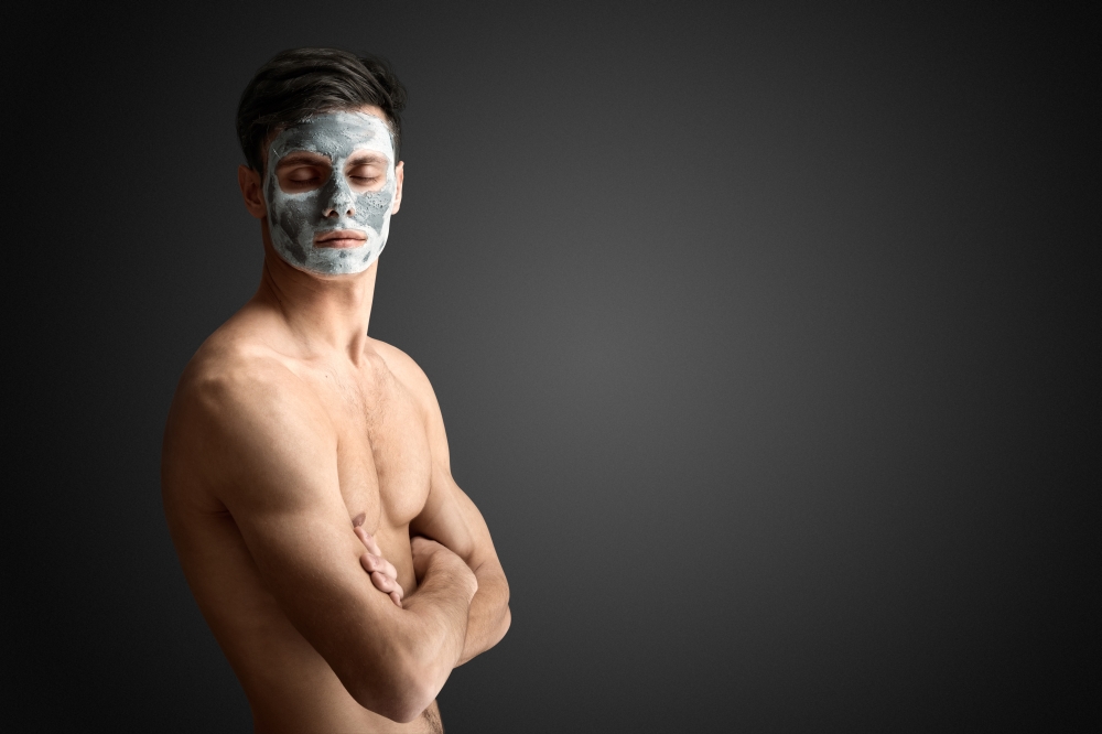 Portrait of a beautiful young man with a facial mud clay mask, face and body skin care treatment.