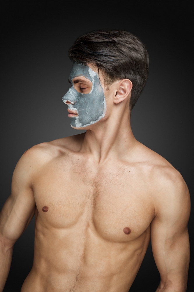 Portrait of a beautiful young man with a facial mud clay mask, face and body skin care treatment.