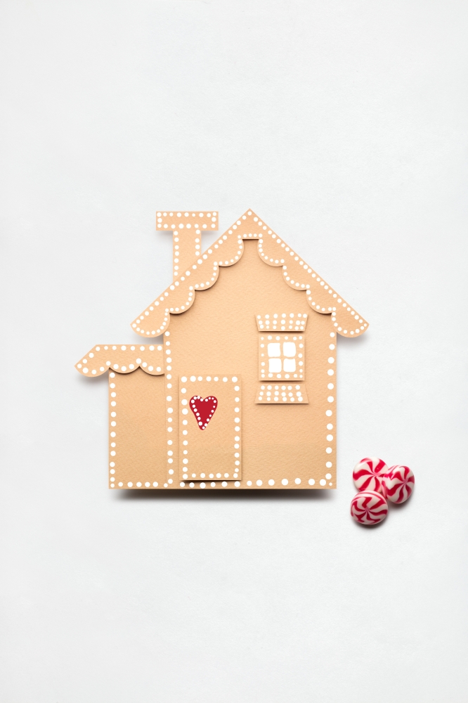 Creative concept photo of a paper house with christmas candies on white background.