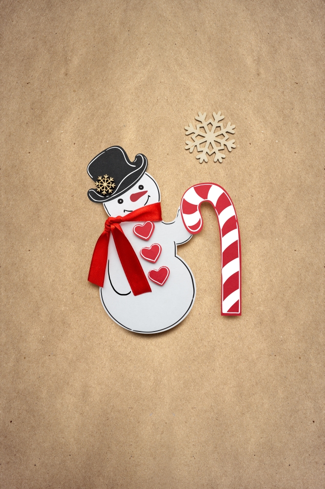 Creative photo of a snowman with a candy made of paper on brown background.