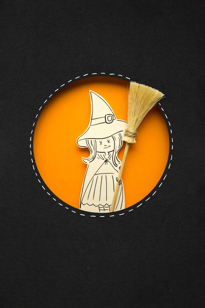 Creative halloween concept photo of witch with broom made of paper on black orange background.