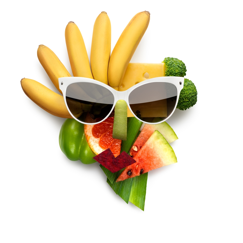 Quirky food concept of cubist style female face in sunglasses made of fruits and vegetables, on white background.