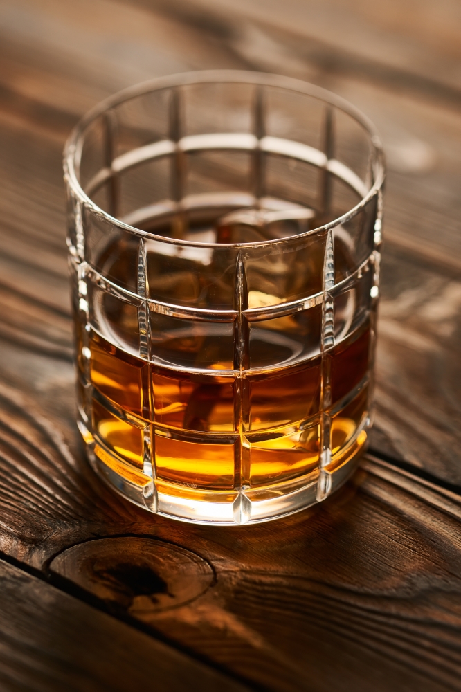 Glass of whiskey with ice cubes on wooden table. Glass of whiskey with ice cubes on rustic wooden table