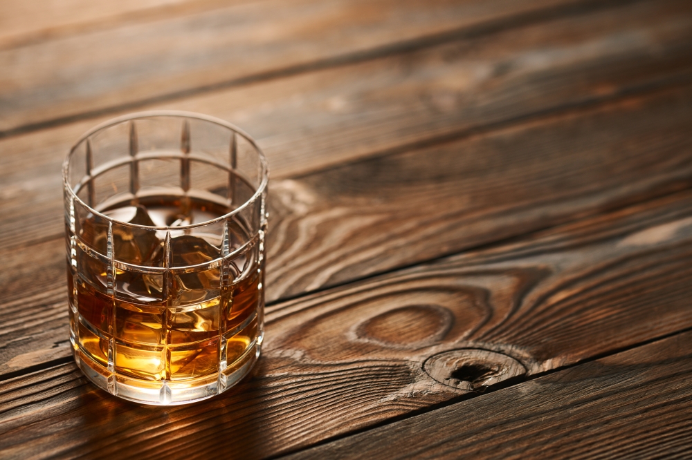 Glass of whiskey with ice cubes on wooden table. Glass of whiskey with ice cubes on rustic wooden table with copy-space