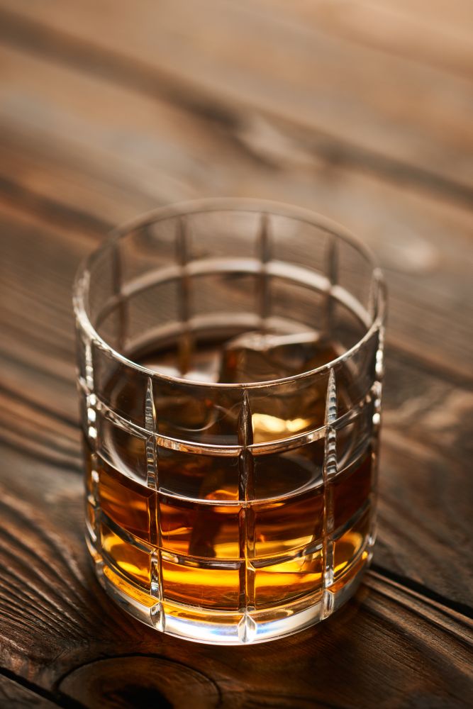 Glass of whiskey with ice cubes on rustic wooden table