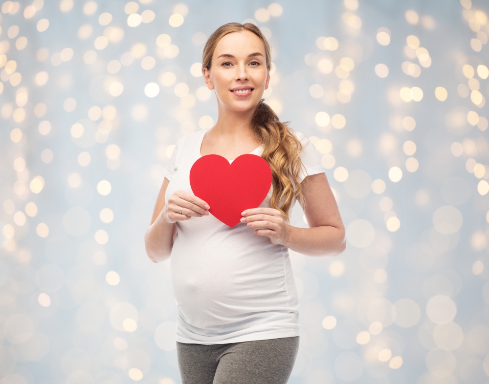 pregnancy, love, people and expectation concept - happy pregnant woman with red heart over holidays lights background. happy pregnant woman with red heart