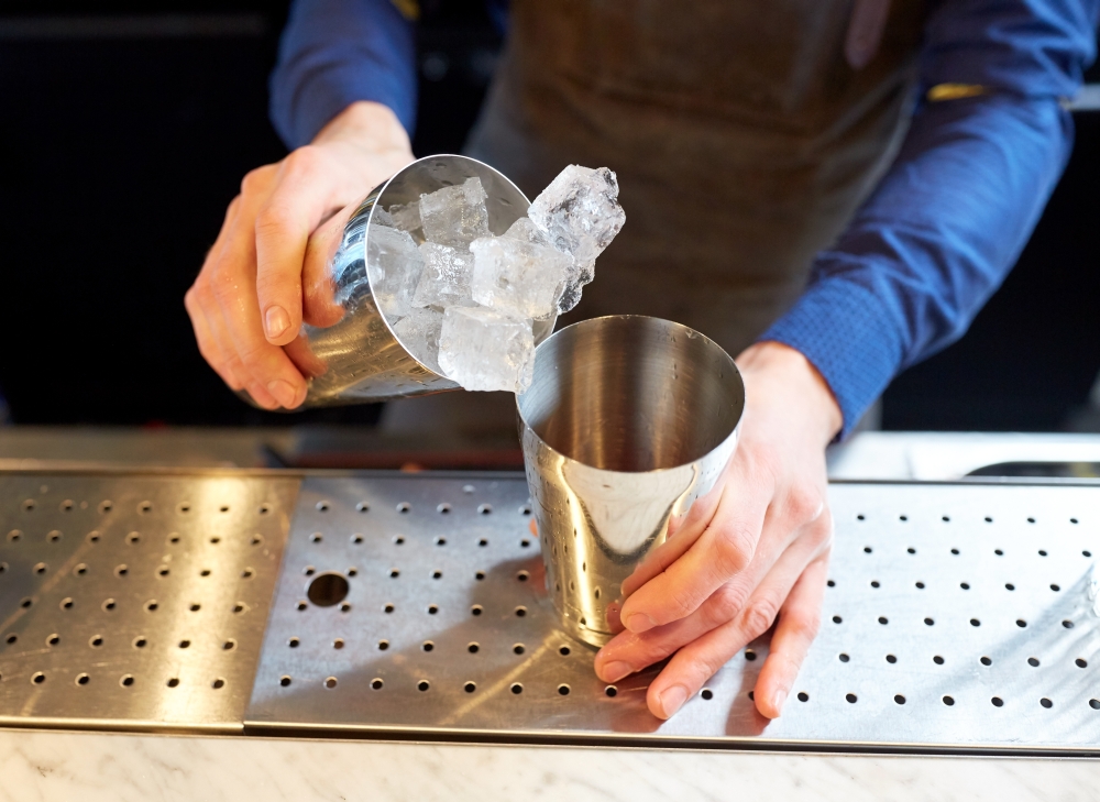 alcohol drinks, people and luxury concept - bartender adding ice into shaker preparing cocktail at bar. bartender with ice and shaker at cocktail bar