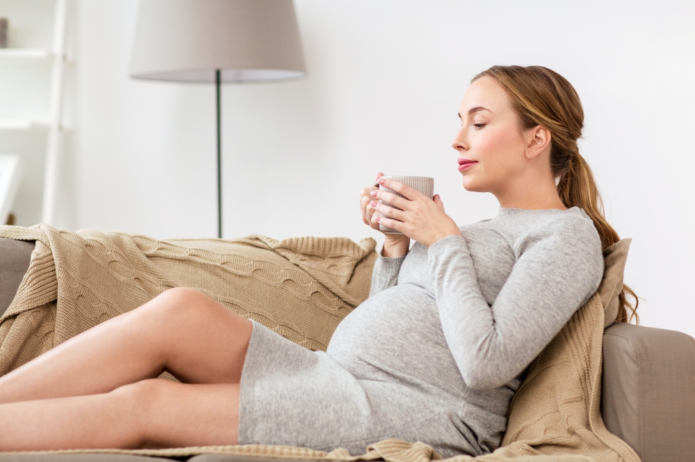 pregnancy, drinks, rest, people and expectation concept - happy pregnant woman with cup drinking tea at home. happy pregnant woman with cup drinking tea at home