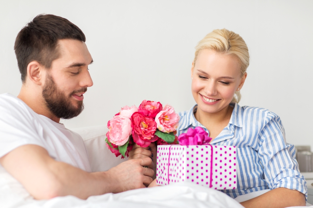 holidays, birthday, valentines day, romance and people concept - happy couple with gift box in bed at home. happy couple with gift box in bed at home