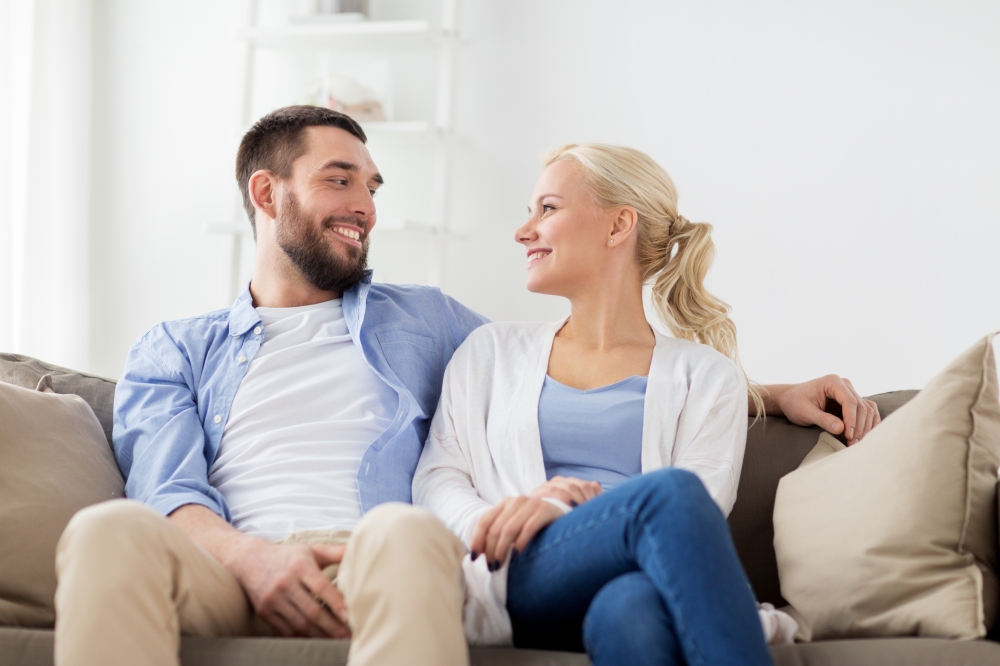 love, family and people concept - smiling happy couple sitting on sofa at home. smiling happy couple sitting on sofa at home