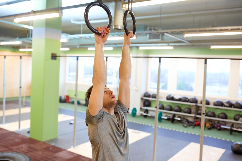 sport, fitness, training and people concept - man exercising and doing ring pull-ups in gym. man exercising and doing ring pull-ups in gym