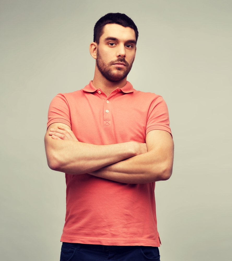 people concept - young man in polo t-shirt with crossed arms over gray background. young man with crossed arms over gray background