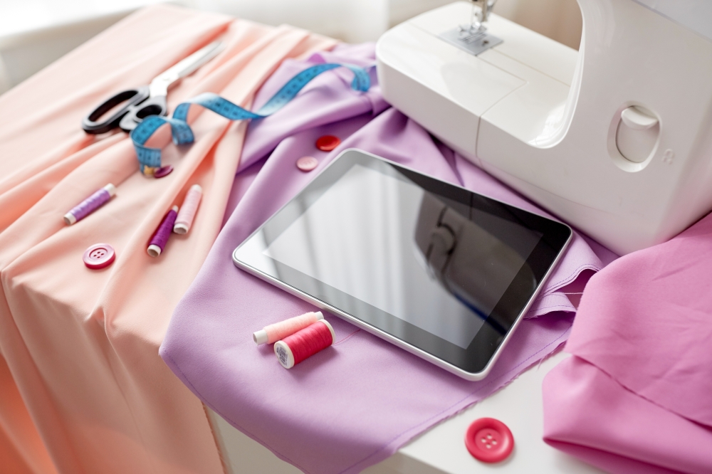 needlework, technology and tailoring concept - sewing machine with tablet pc computer, scissors, tape measure and fabric. sewing machine, tablet pc, scissors and ruler