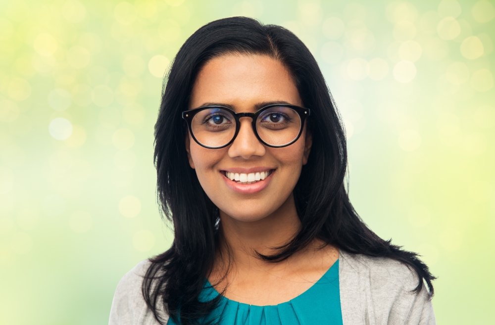 vision, portrait and people concept - happy smiling young indian woman in glasses over green background with lights. happy smiling young indian woman in glasses