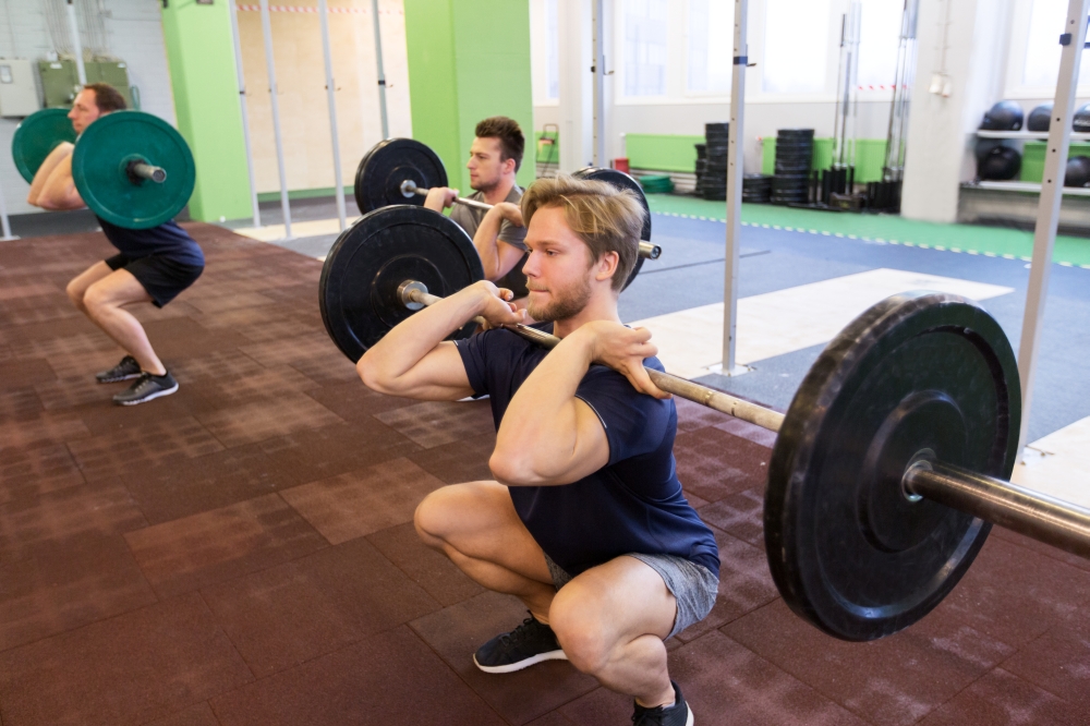 fitness, sport and people concept - men with barbells doing squats at group training in gym. group of men training with barbells in gym