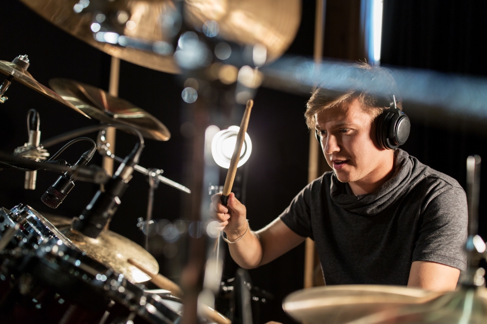 music, people, musical instruments and entertainment concept - male musician in headphones with drumsticks playing drums and cymbals at concert or studio. male musician playing drums and cymbals at concert