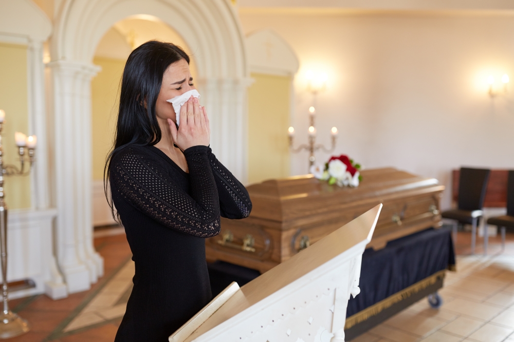 burial, people, grief and mourning concept - close up of sad woman with napkin crying near coffin at funeral in church. woman crying near coffin at funeral in church