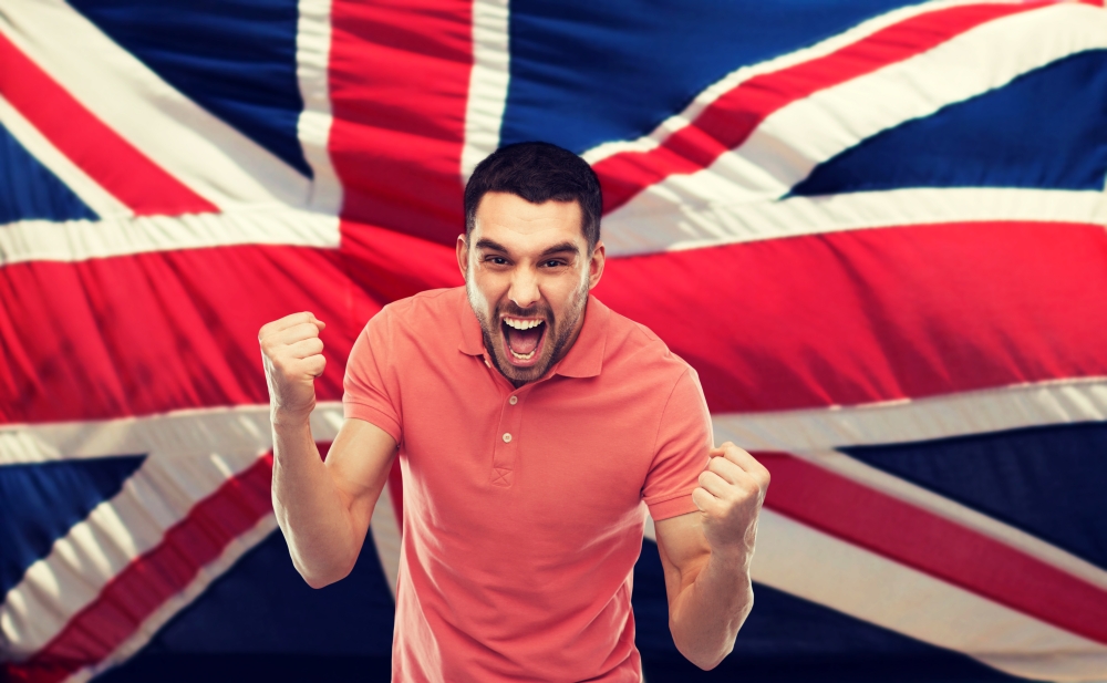 emotion, aggression, patriotism, gesture and people concept - angry young man showing fists and shouting over brittish flag. angry man showing fists over brittish flag